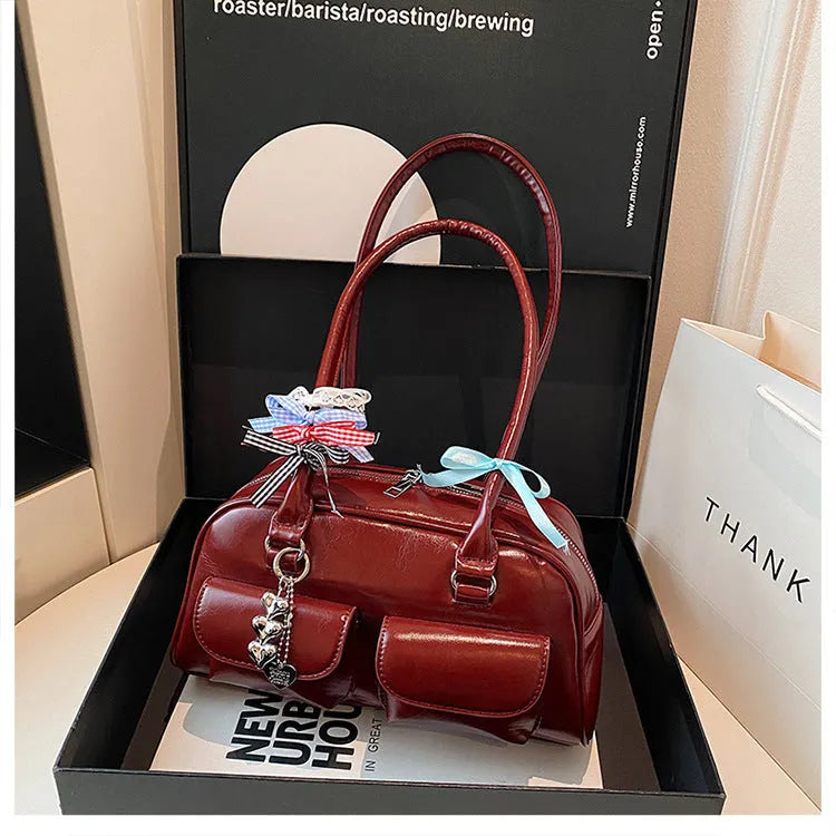 Retro-style brown PU leather women's pillow handbag with a one-shoulder strap, shown with a decorative ribbon pendant.