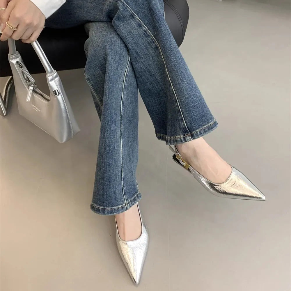 Women's black pointed toe leather shoes with a thin low heel and ankle strap on a rubber sole.