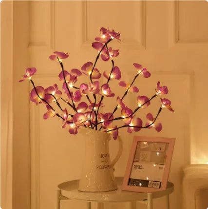 Pink fabric and plastic LED Phalaenopsis orchid branch light, 65cm long, on a table providing warm white ambient glow.