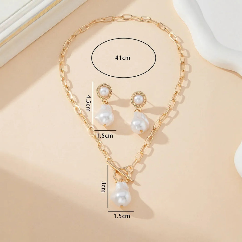 Gold-coloured baroque pearl pendant necklace and earring set on a dark background.