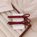 Wine red genuine leather bow hair clip on a dark background, showing metal clasp.