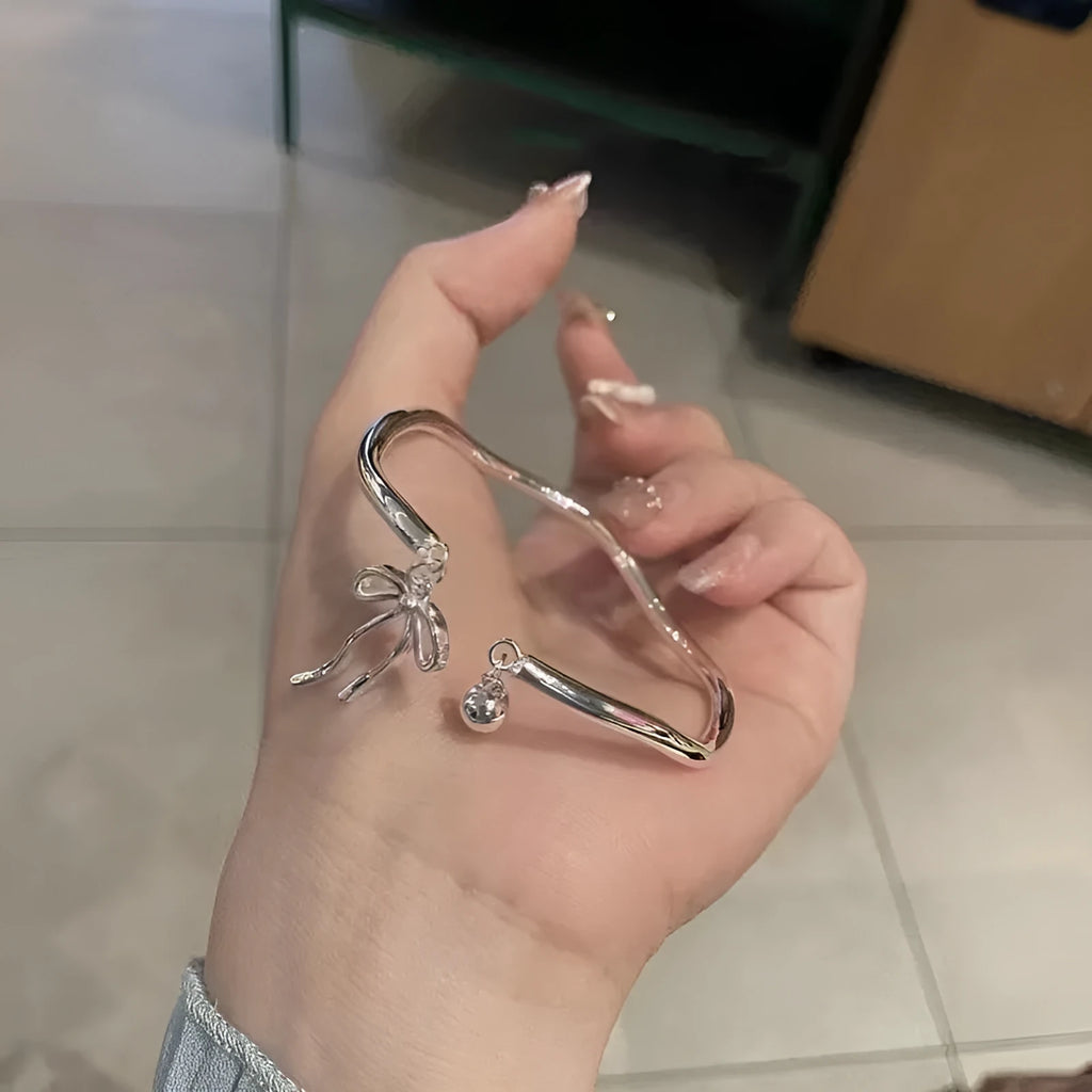 Silver adjustable bracelet with a detailed opening bow charm on a model's wrist, showing the lobster clasp.