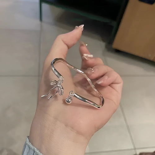 Silver adjustable bracelet with a detailed opening bow charm on a model's wrist, showing the lobster clasp.