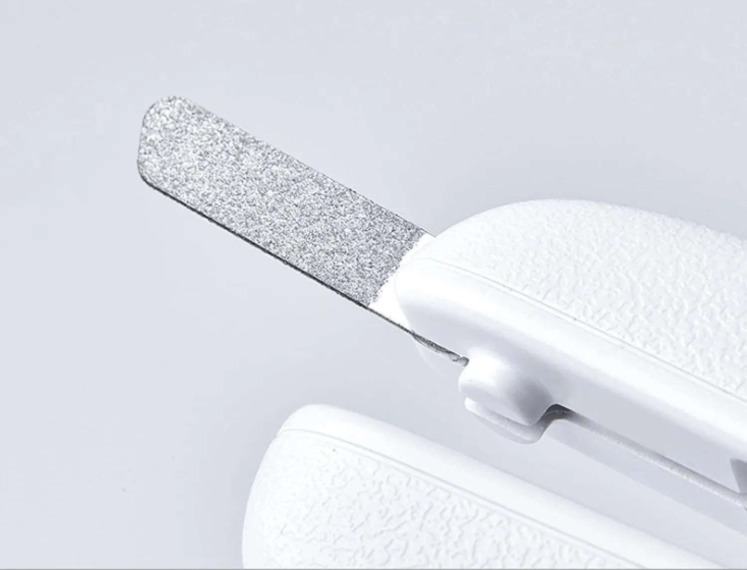 White pet nail clippers with LED light and transparent anti-splash guard next to a nail file on a table