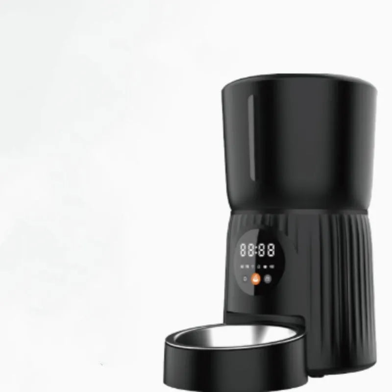 Black automatic pet feeder with digital timer display and remote control on a table.