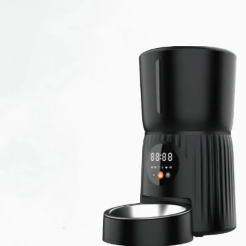 Black automatic pet feeder with digital timer display and remote control on a table.
