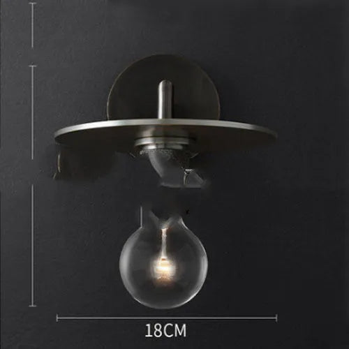 Gold bronze or black wall lamp with triangular transparent glass shade and wrought iron frame for bedside or hallway use