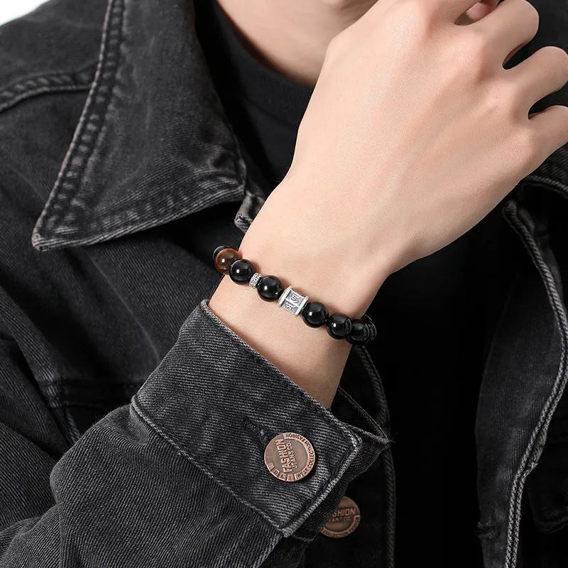 Black obsidian prayer wheel bracelet for men with a hand-woven silver clasp on a wrist.