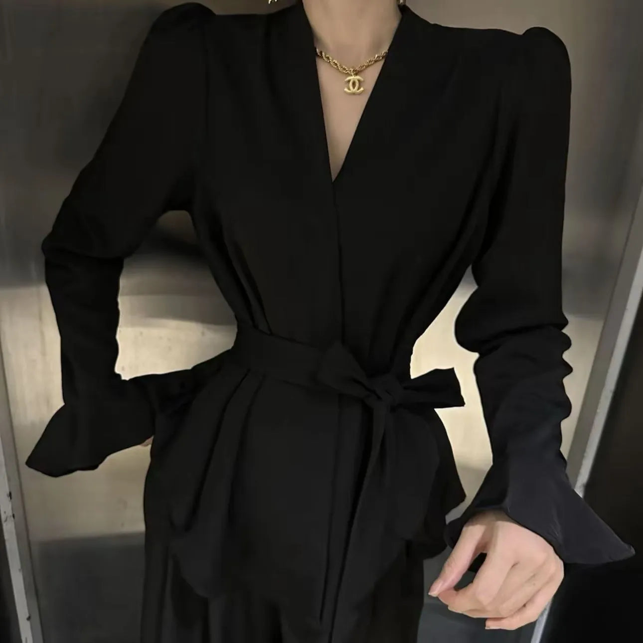 A woman wearing a black French-style shirt with an irregular collar and long bell sleeves.