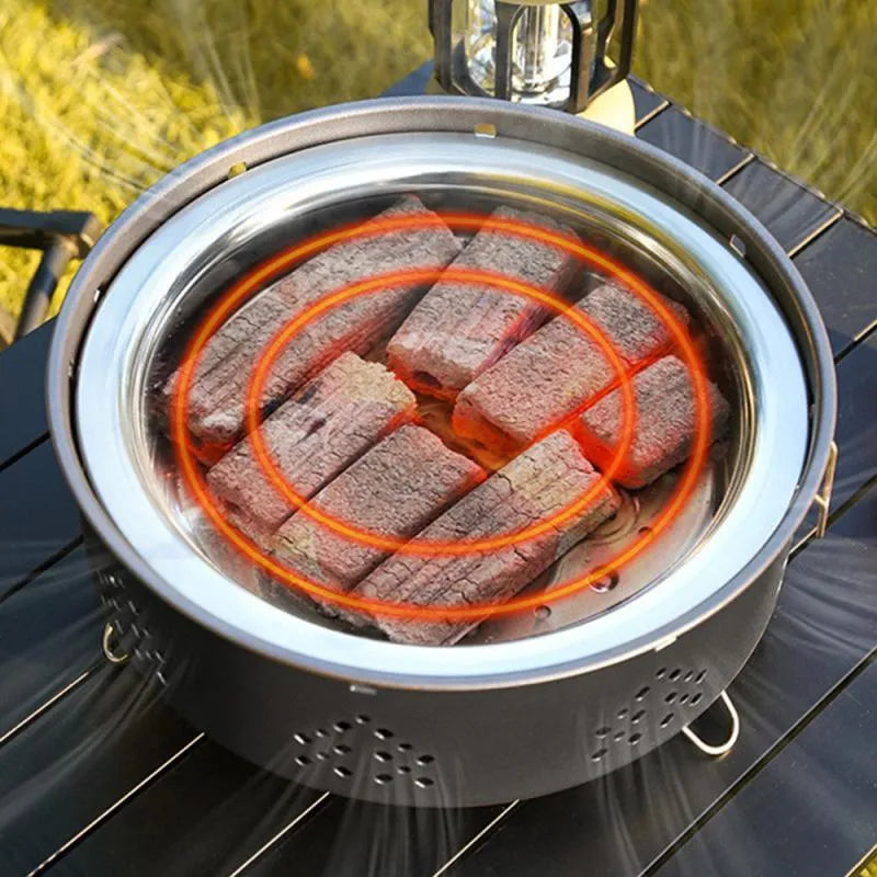 Portable stainless steel barbecue grill with detachable parts on a grassy outdoor surface.