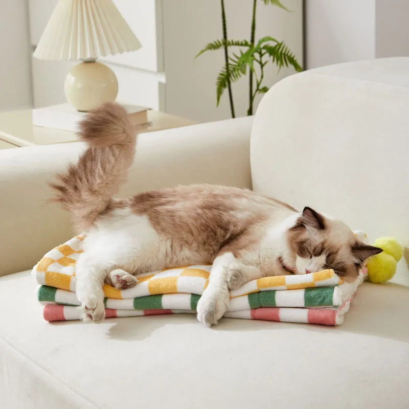 Green plaid pattern fleece pet blanket with a fur ball decoration, shown on a sofa.