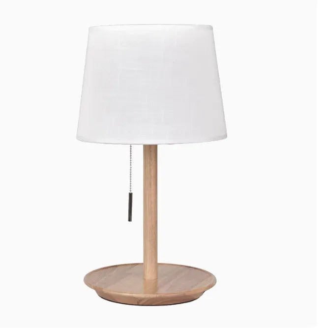 Walnut-coloured solid wood bedside lamp with a white cloth shade on a wooden surface.