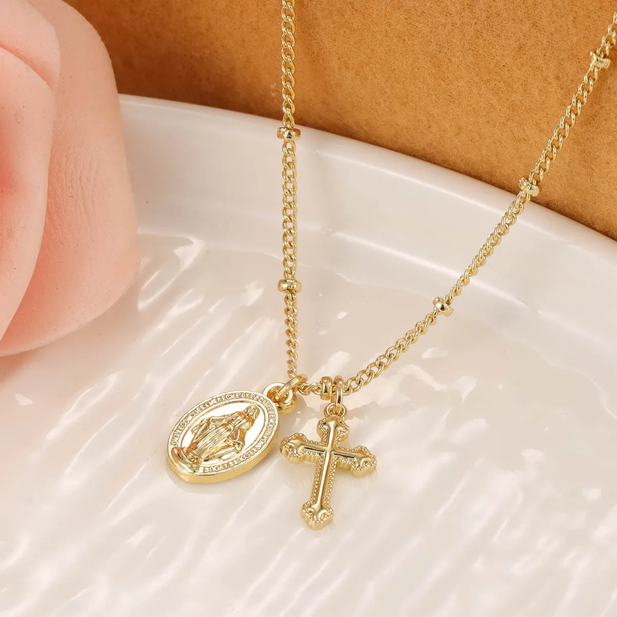 Geometric gold Virgin Mary and cross pendant necklace on a chain, showing minimalist design.