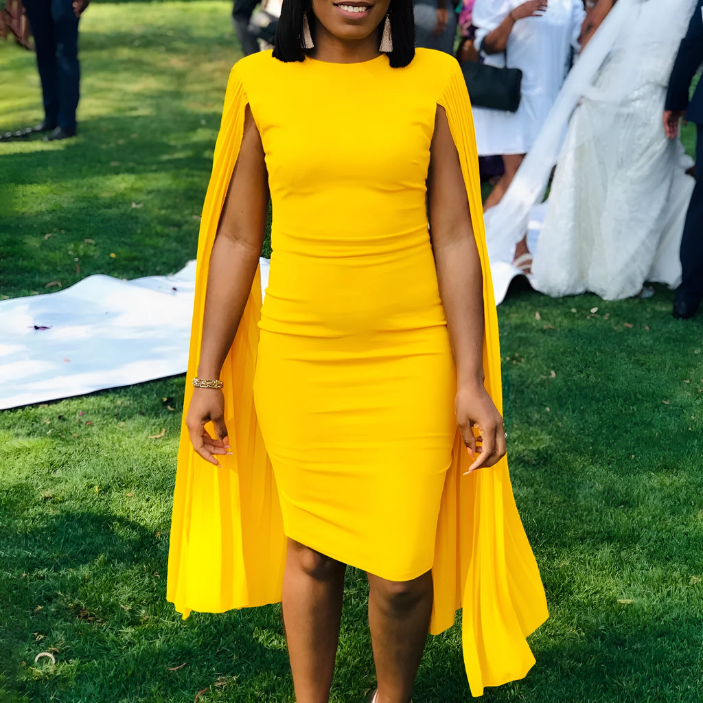 Yellow high-waisted evening gown with long sleeves and a full pleated skirt, model standing formally.
