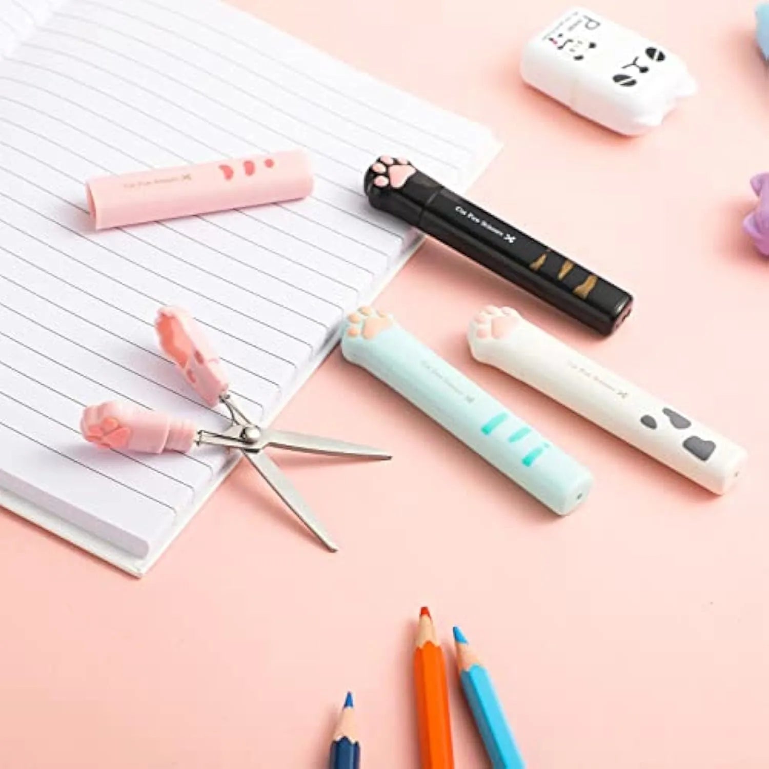 Set of four mini folding scissors with cat paw design in black, blue, pink, and white colours on a plain surface.
