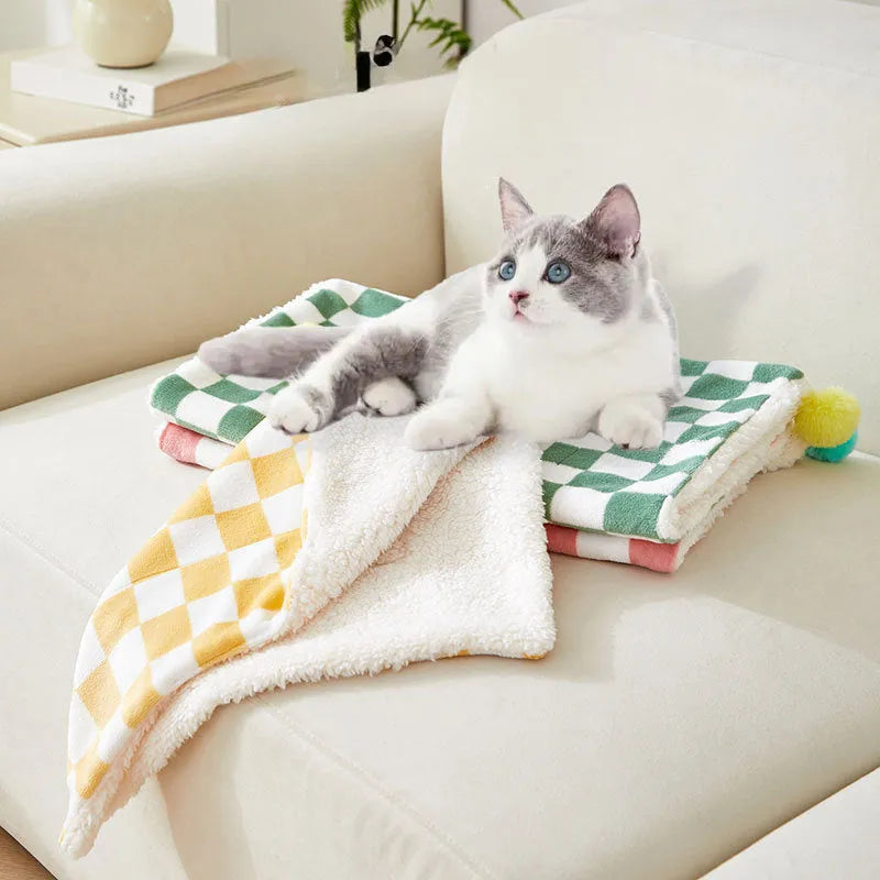 Green plaid pattern fleece pet blanket with a fur ball decoration, shown on a sofa.