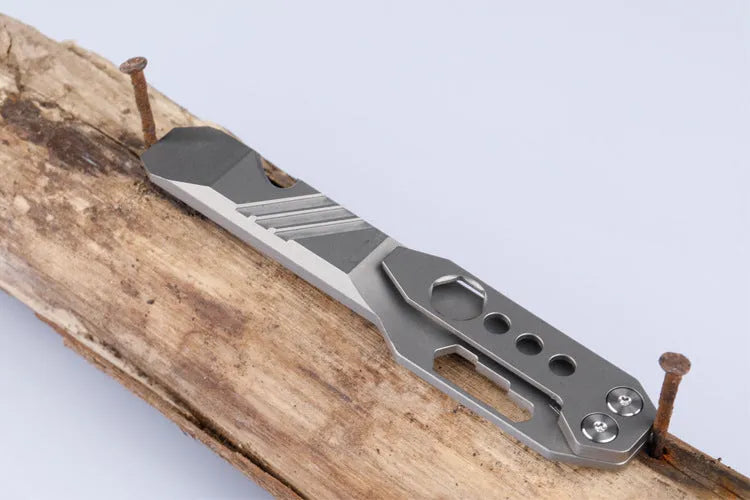 Titanium alloy multi-tool with crowbar edge, screwdriver tip, and bottle opener notches on a stone wash finish background.