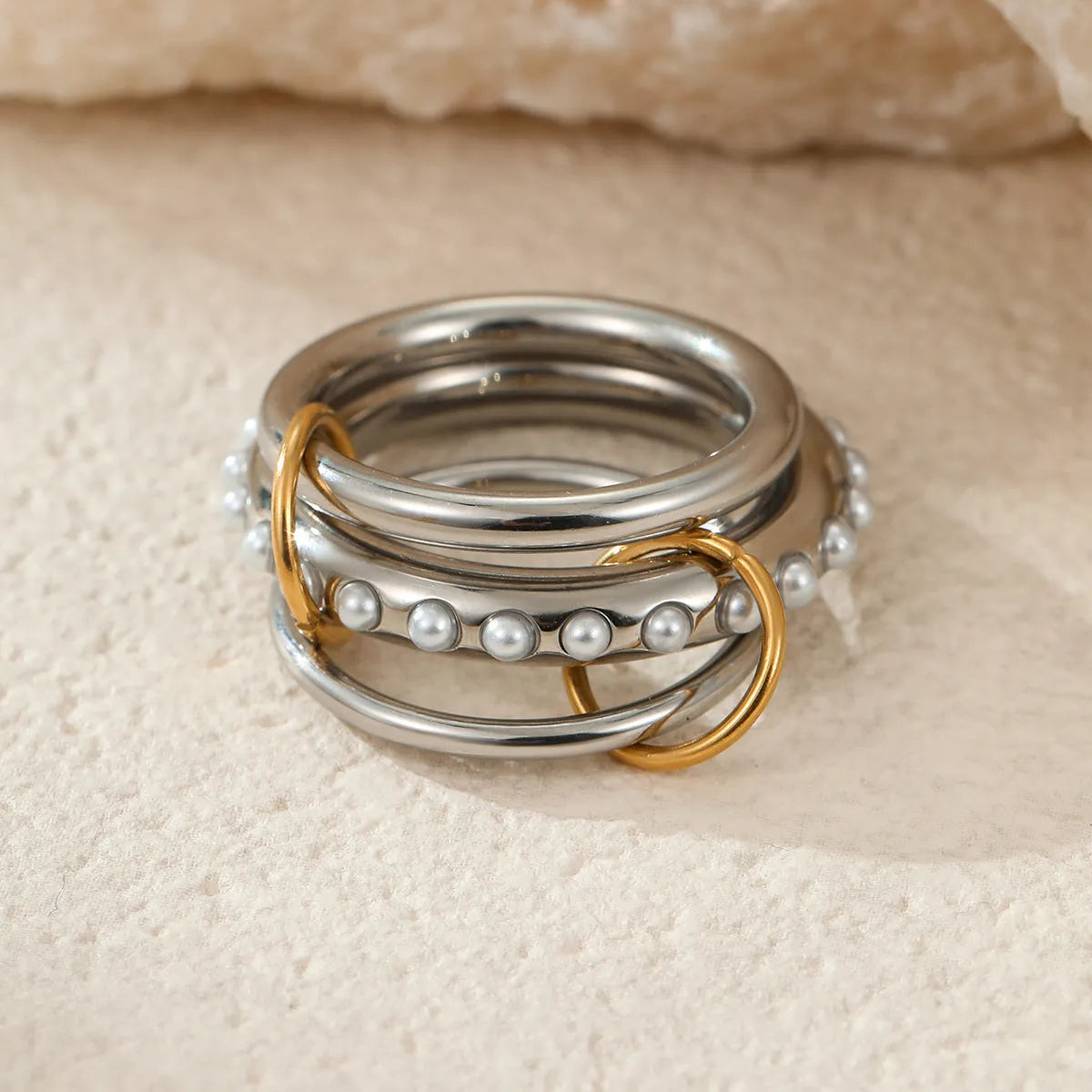 Stacked gold plated stainless steel rings with an exaggerated design on a person's hand.