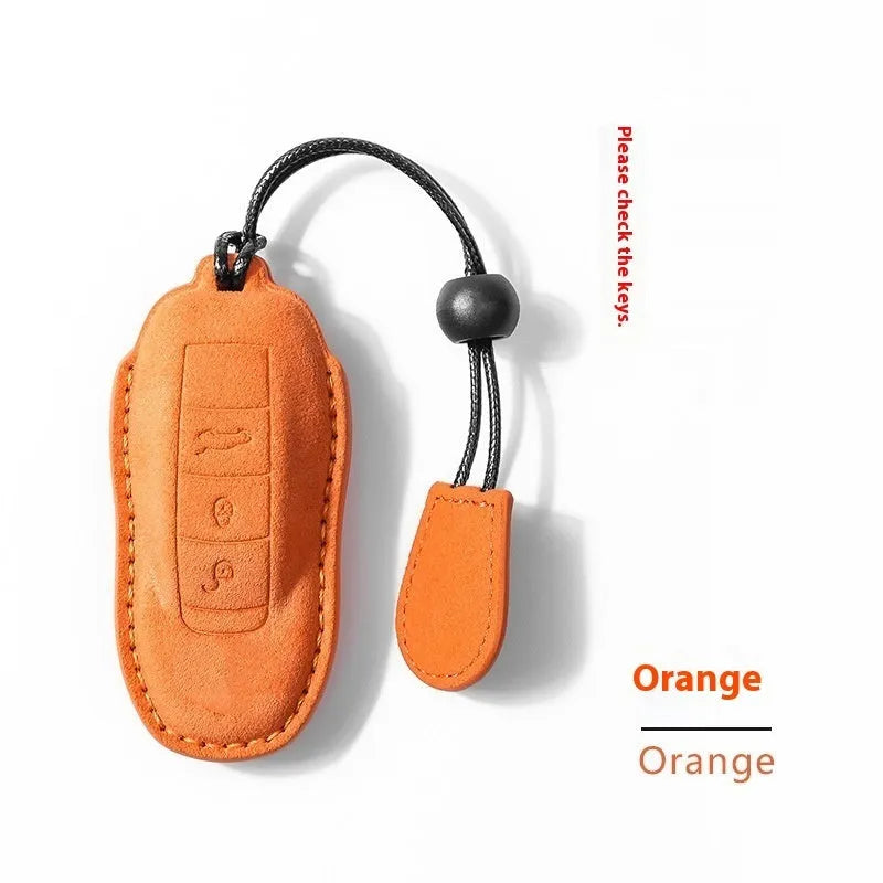 Suede car key cover in cement grey, dark green, light grey, and orange colour options on a plain background.