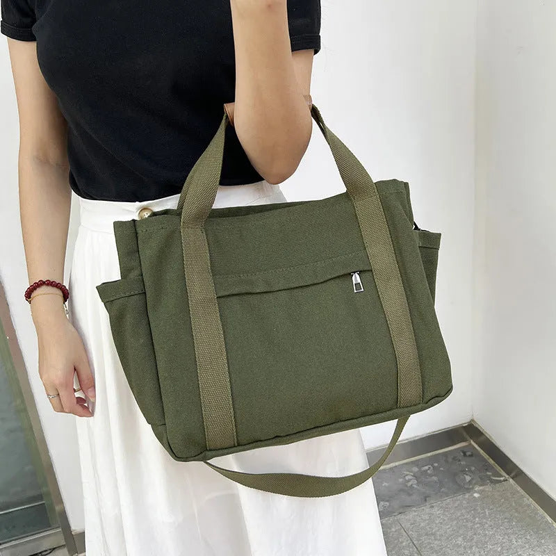 A horizontal square canvas tote bag in army green with a cross-body strap and visible sewing lines.