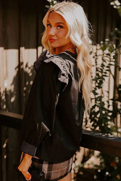 Black women's V-neck blouse with ruffle detailing on the long sleeves and contrast stitching.