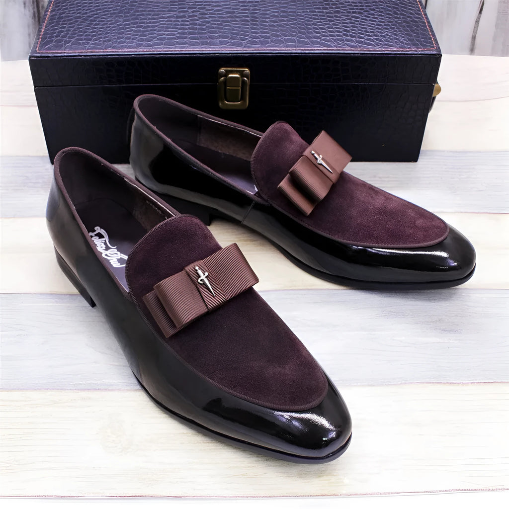 Men's black and brown tassel loafers with a matte and patent leather upper on a wooden floor.