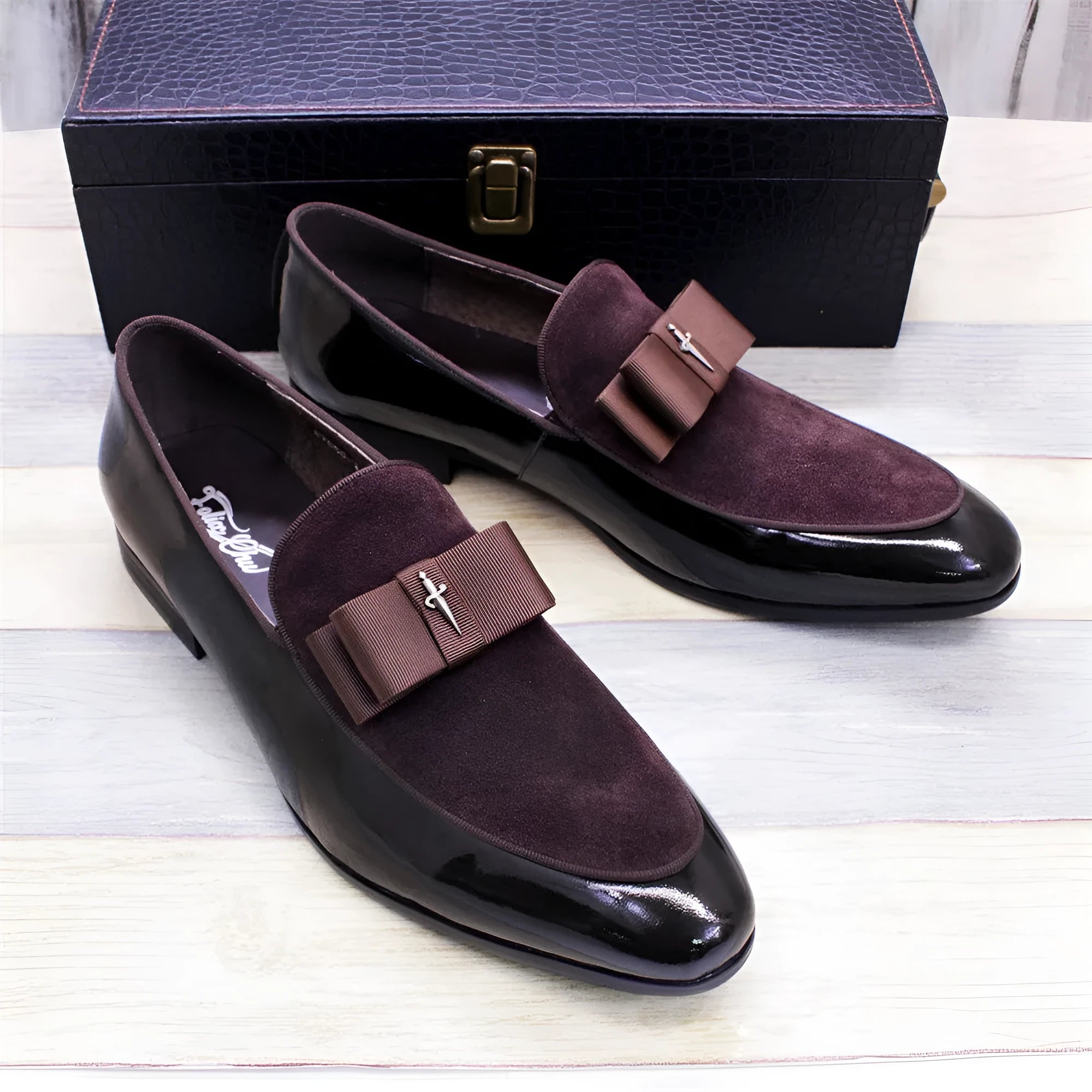 Men's black and brown tassel loafers with a matte and patent leather upper on a wooden floor.
