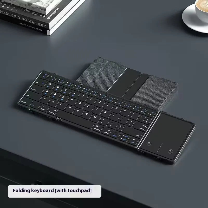 Black folding Bluetooth keyboard showing compact folded size beside mobile phone