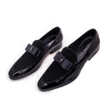 Men's black and brown tassel loafers with a matte and patent leather upper on a wooden floor.