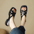 Women's black patent leather square toe sandals with a cross strap and low heel on a white background.