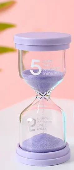 Handmade glass sand timer in blue colour showing sand flowing, on a wooden desk.