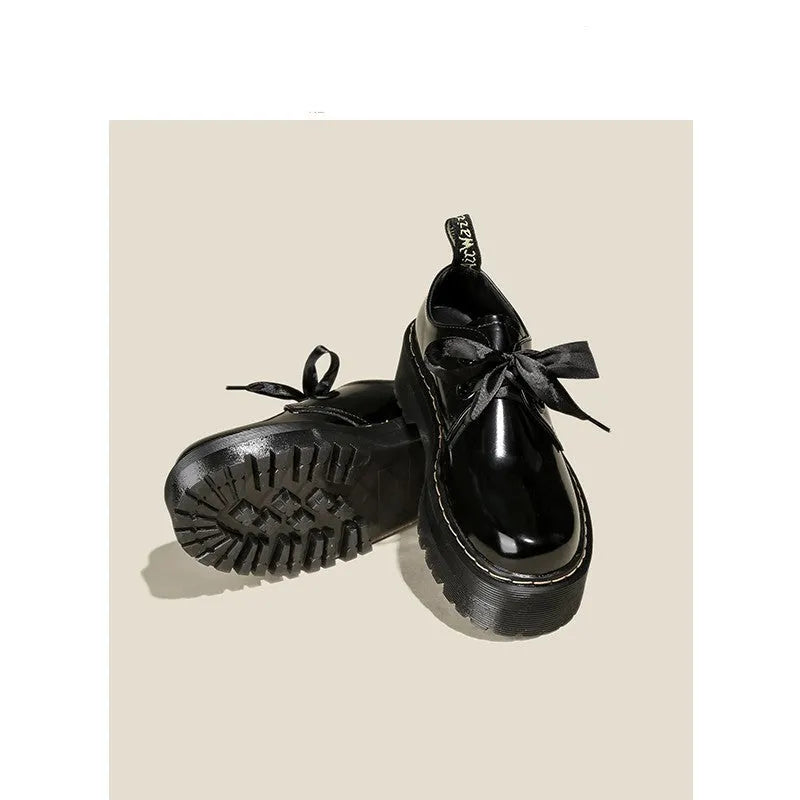 Women's black leather shoes with a thick sole, cross straps, and ribbon laces laid flat.
