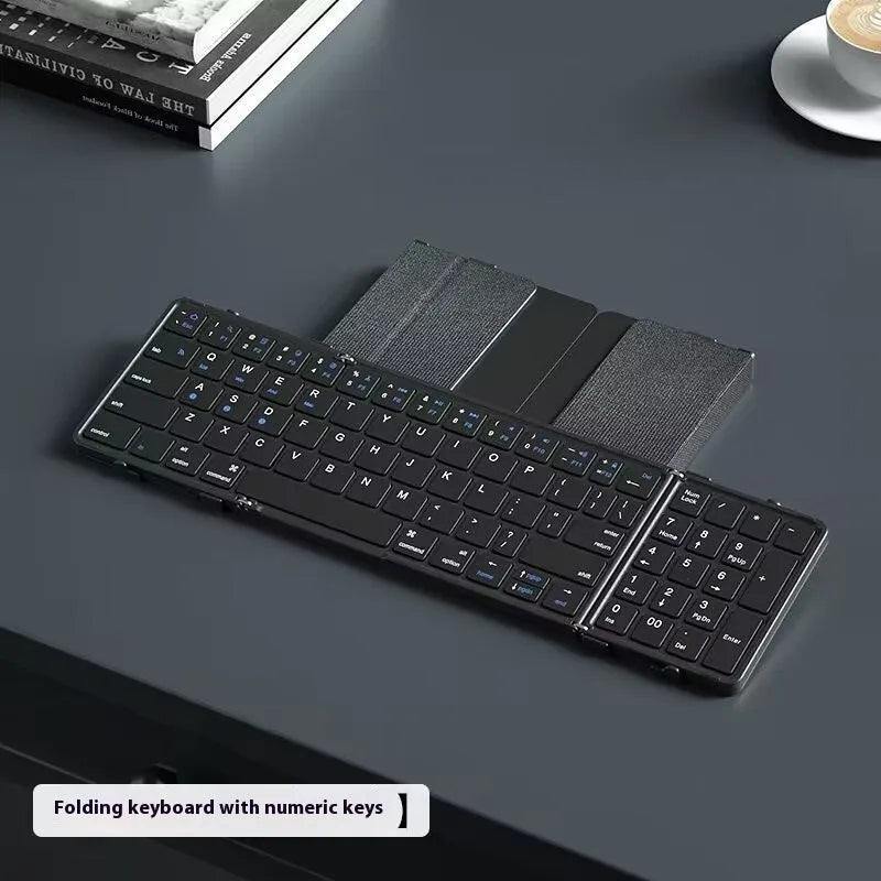 Black folding Bluetooth keyboard showing compact folded size beside mobile phone