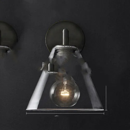 Gold bronze or black wall lamp with triangular transparent glass shade and wrought iron frame for bedside or hallway use