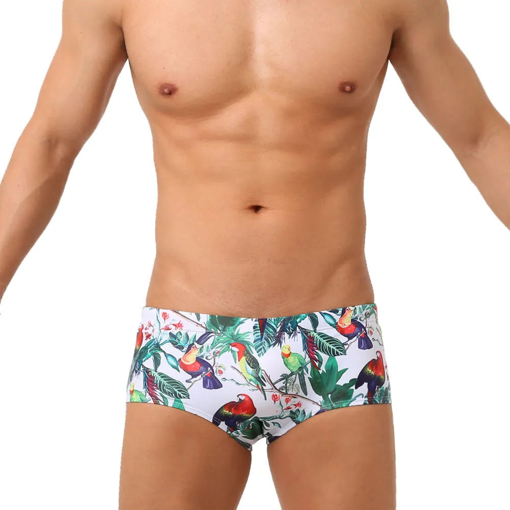 Men's blue swimming trunks with a detailed floral and bird print pattern, small boxer style