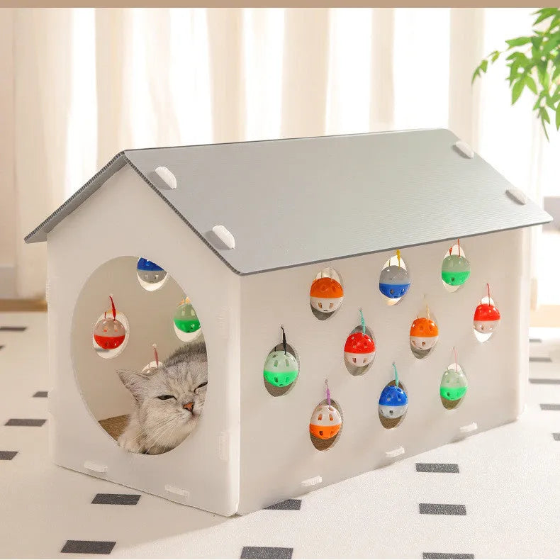 White plastic house-shaped cat scratch board with sisal siding, an arched tunnel entrance, and a dangling red bell ball toy.