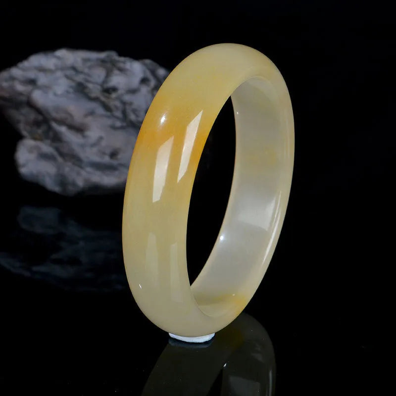 A polished light jade bracelet in a classic Chinese style band design on a plain background.