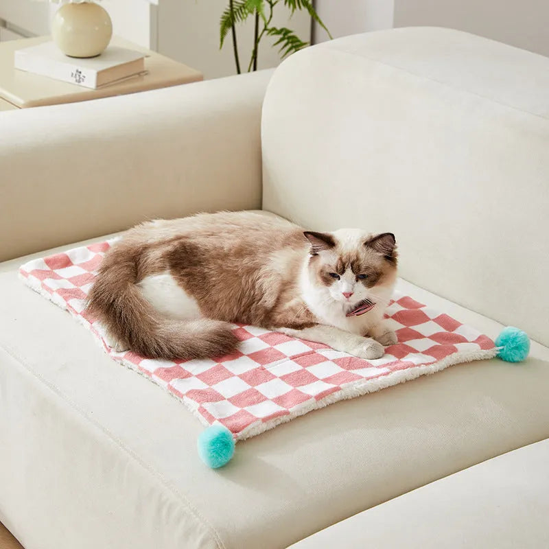 Green plaid pattern fleece pet blanket with a fur ball decoration, shown on a sofa.