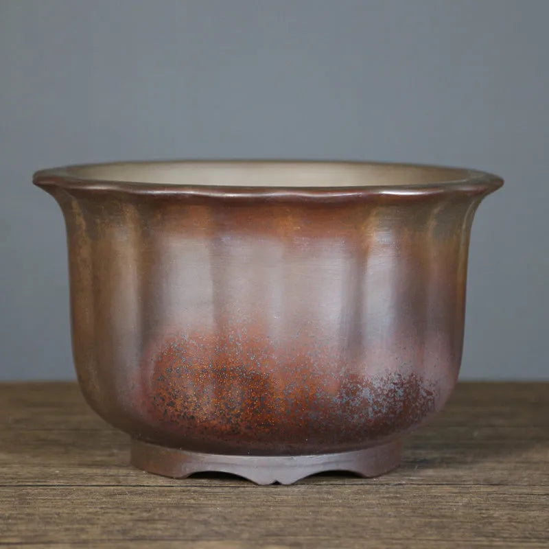 Antique carved ceramic flower pot with wood burning finish on a wooden table.