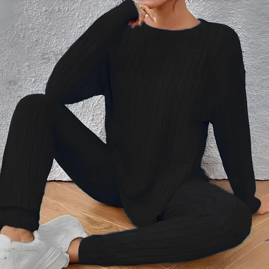 A woman wearing a black sunken stripe two-piece loungewear set, consisting of a regular-sleeve top and elasticated waist trousers.