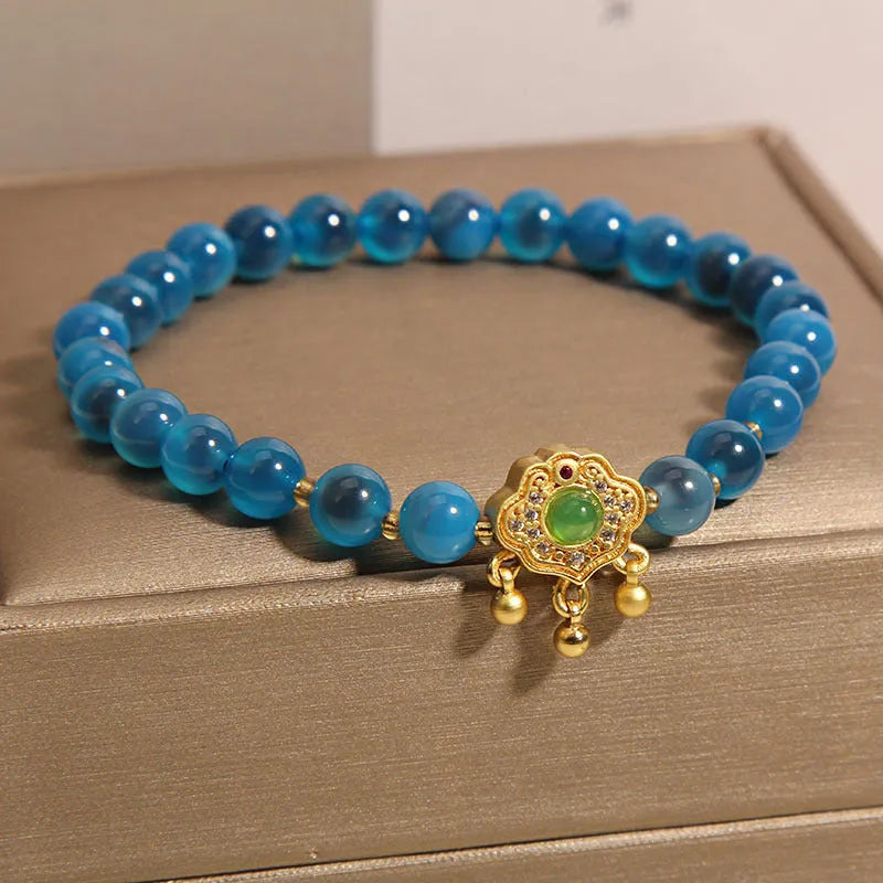 Blue sugar heart agate safety lock pendant on women's bracelet with alloy inlay and crystal accents.