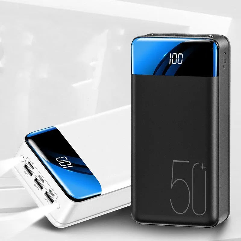 Black and white large 50000mAh portable power bank with multiple USB ports, showing scale next to a smartphone.