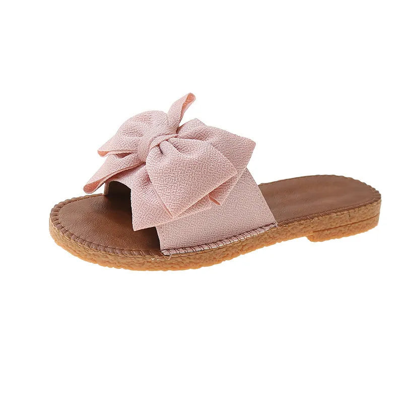 Women's beige slip-on cloth sandals with a bow on the upper and a soft flat rubber sole.