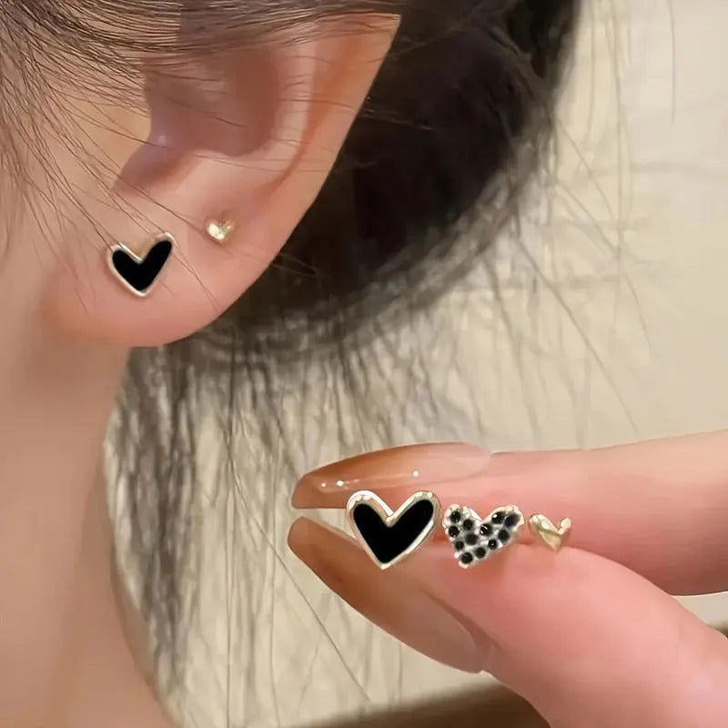 Three pairs of heart-shaped earrings in gold, black, black-white, and pink colours on display