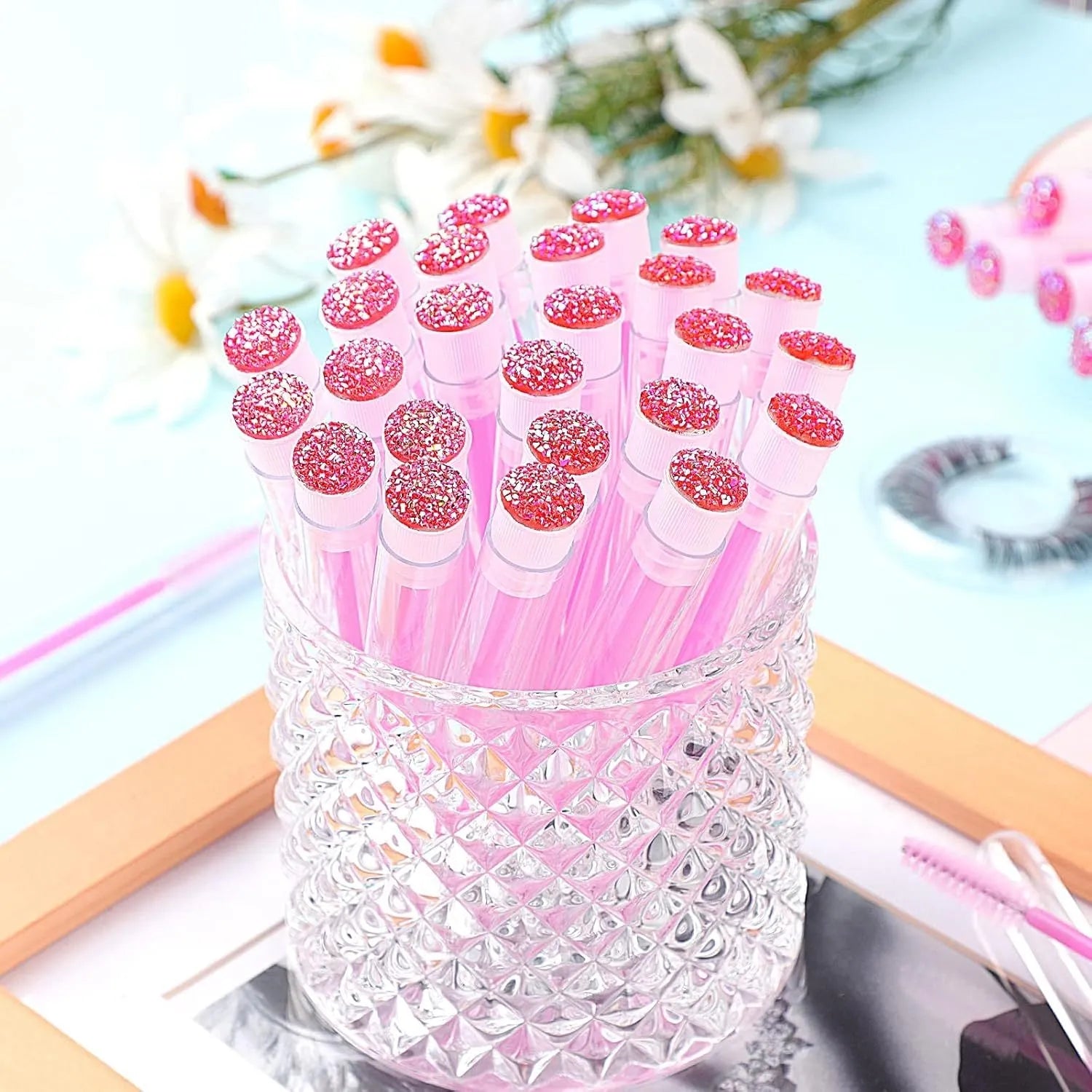 Set of coloured disposable mascara brushes inside clear plastic storage tubes on a white background.