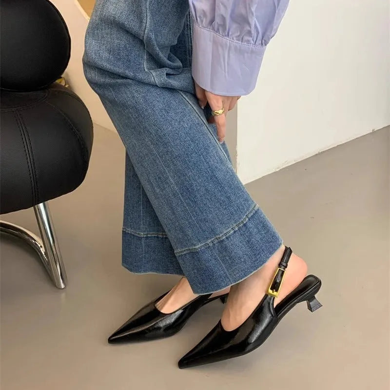 Women's black pointed toe leather shoes with a thin low heel and ankle strap on a rubber sole.