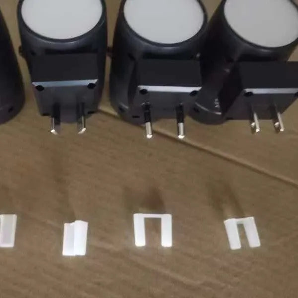 A small white plug-in night light with an adjustable head, shown next to a power socket for scale.