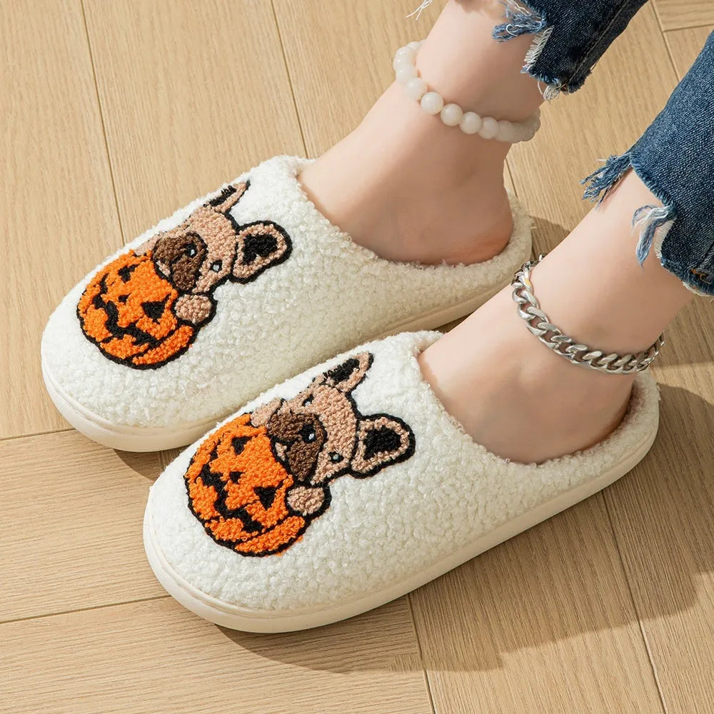 Black Halloween slippers with pumpkin print, plush fabric, and thick textured TPR rubber soles on a wooden floor.
