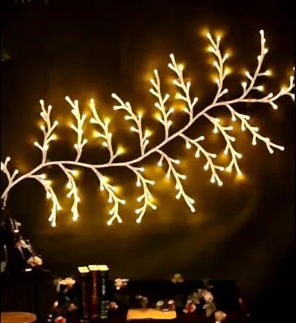 Flexible plastic LED willow vine garland with warm white lights bent into a decorative shape on a wall.