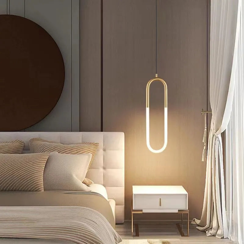 Modern Nordic-style U-shaped metal pendant light with a long black cable, hung above a bedside table.